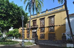 Edificio de dos plantas con ventanas de madera y balcón en la calle.