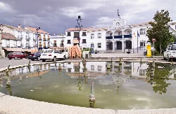 Plaza con estanque, edificios blancos y un ayuntamiento en Hinojosa del Duque.