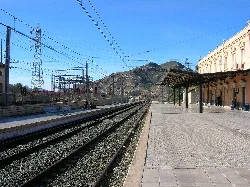 Train tracks and platform at Elda station with mountains in the background.