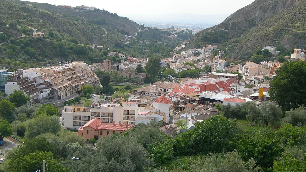 Panoramablick auf Monachil in Granada, mit Häusern und Straßen im Tal, umgeben von Bergen und Vegetation.