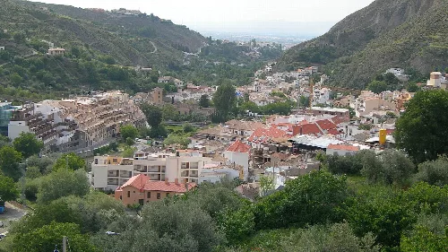 Panoramablick auf Monachil in Granada, mit Häusern und Straßen im Tal, umgeben von Bergen und Vegetation.