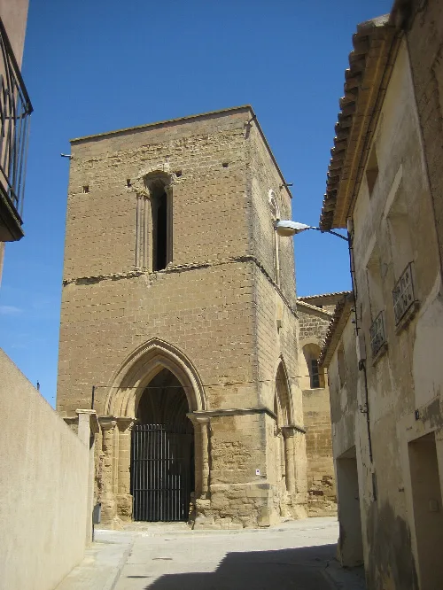 Se trata de una iglesia construida en el s.XII en estilo románico
tardío, que debido a su importancia llegó a ostentar el rango
de colegiata. Su fábrica es de sillar y actualmente se encuentra
exenta.
Consta de tres naves y cabecera triple con ábsides semicirculares
cubiertos por bóveda de horno. Las naves se cubren con
bóvedas de cañón y el crucero, no marcado en planta, con
bóveda de crucería estrellada del s.XVI.
También de época renacentista data la construcción del coro
alto situado a los pies de la nave central y de la capilla de San
Pedro Arbués, situada junto al coro.
Su portada principal se abre en el muro septentrional y junto a
ella existe una ventana sobre la que hay embutido un tímpano
tallado con un Pantocrátor rodeado por el Tetramorfos y un
crismón trinitario.
En el muro meridional se encuentra adosado un gran atrio
abierto por medio de tres arcos apuntados y cubierto por una
bóveda de crucería sencilla. Las columnas situadas en los ángulos
del atrio presentan bellos capiteles historiados.
Sobre este atrio se alza una magnífica torre del s.XIII, de planta
cuadrada y dos cuerpos en altura rematados por una terraza
plana.

Entorno