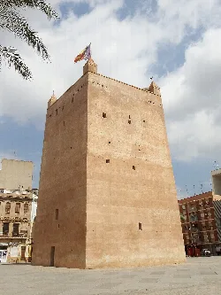 Arab tower of Torrente with flags on top and a cloudy sky.