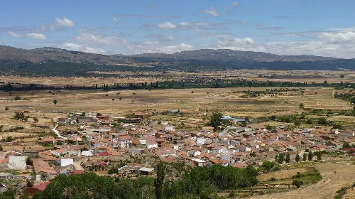 Blick auf ein Dorf mit Häusern und landwirtschaftlichen Feldern in einer offenen Landschaft.