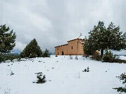 Ermita de la Virgen de la Cabeza en un paisaje nevado con árboles y cielo nublado.