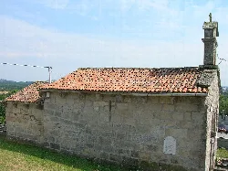 Pequeña iglesia de piedra con tejado de tejas rojas y una chimenea en la esquina.