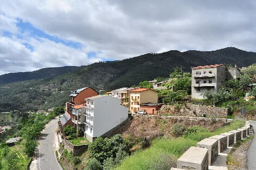 Häuser und Gebäude an einem Hang mit grünen Bergen im Hintergrund.