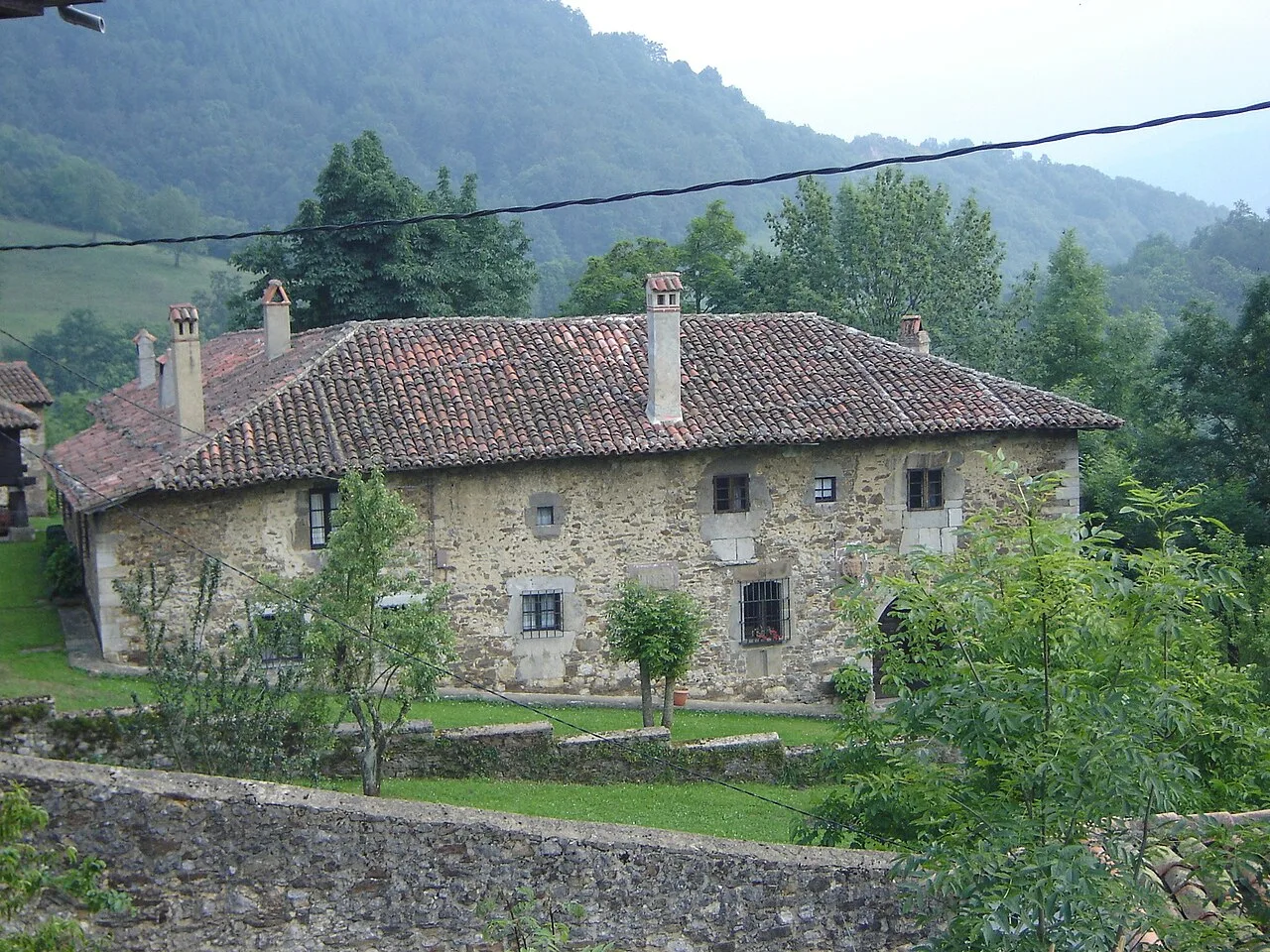 Stone palace with red tile roof and chimneys in a rural setting.