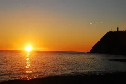 Sonnenuntergang am Strand mit Sonne, Meer und Leuchtturm auf dem Hügel.