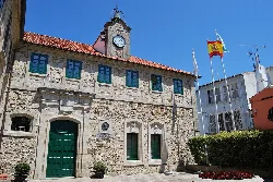 Edificio de piedra con reloj y banderas en la plaza de Ortigueira.