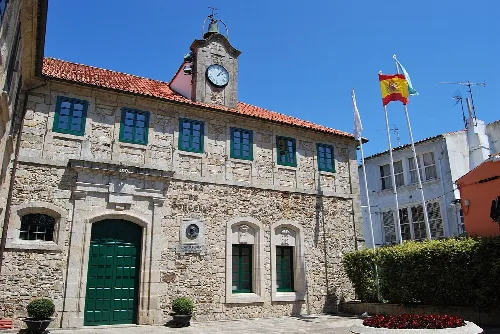 Stone building with clock and flags in Ortigueira's main square.