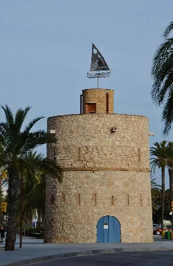 Torre de piedra con puerta azul y mástil con vela decorativa.