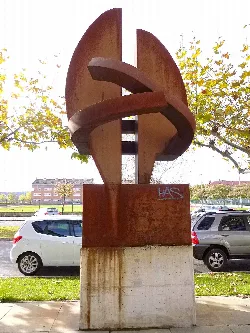 Metallskulptur in einem Park mit Bäumen und Autos dahinter.