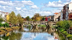 Puente de piedra sobre el río Cabe con edificios y árboles a sus lados.