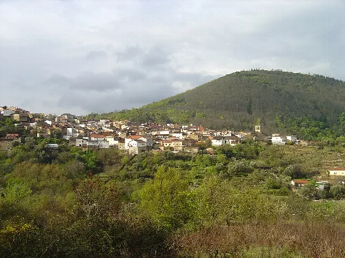 Paisaje con casas en la ladera y un monte verde en el fondo.