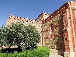Cedillo church with stone and brick walls and a large tree in the foreground.