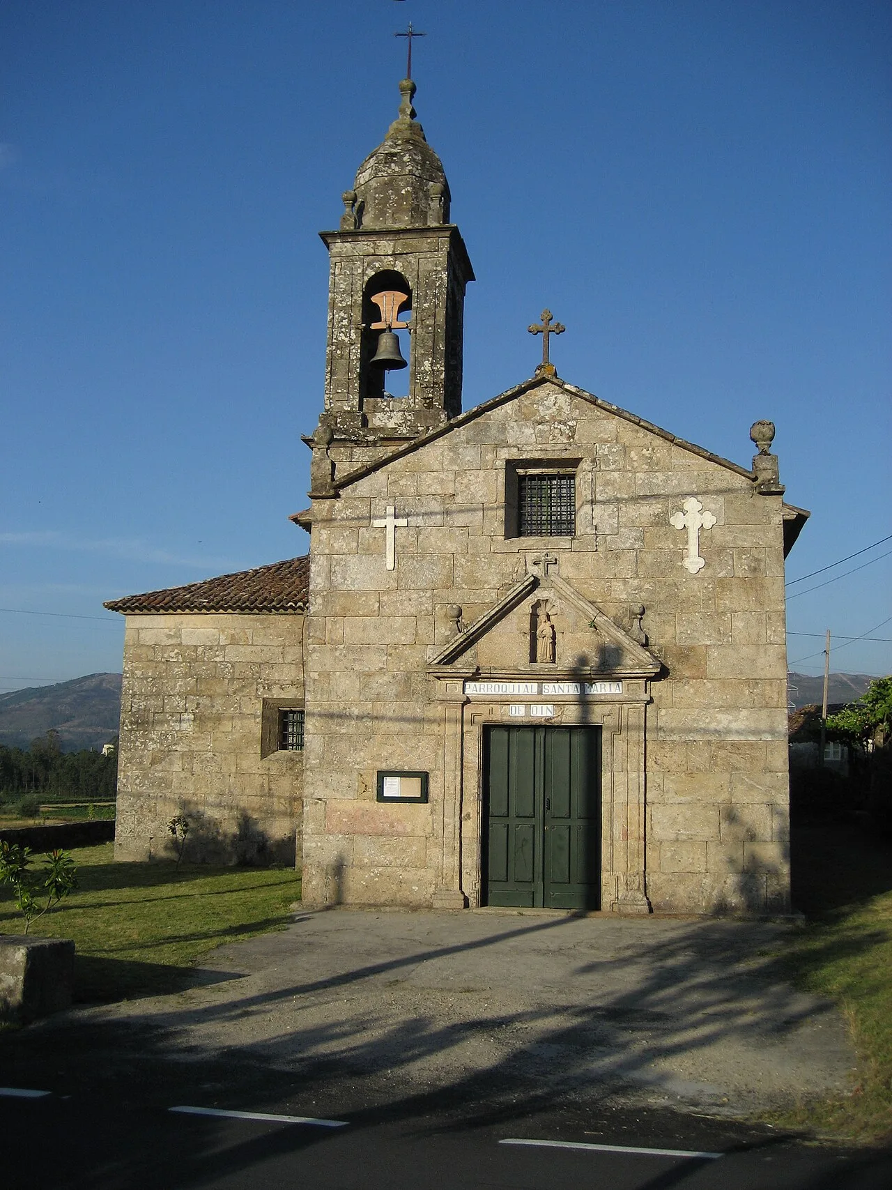 Steinige Kirche mit Glockenturm und Kreuz an der Fassade in Rois, La Coruña.