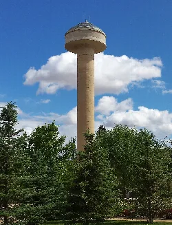 Torre de depósito de agua en un parque rodeado de árboles.
