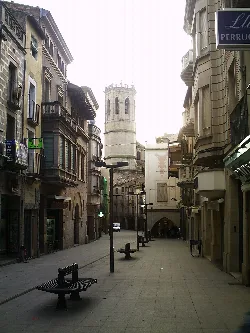 Narrow street with old buildings and a tower in the background in Tárrega.