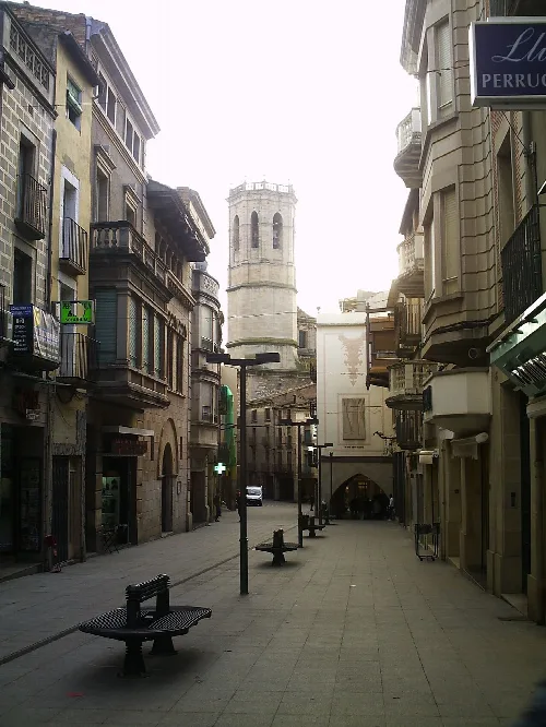 Enge Straße mit alten Gebäuden und einem Turm im Hintergrund in Tárrega.