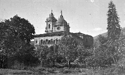 Palacio y torre del jardín con árboles y la iglesia en el fondo.