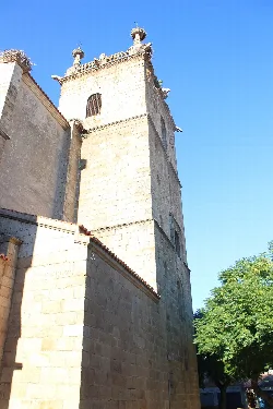 Torre de una iglesia de piedra con detalles decorativos en la parte superior en Casar de Cáceres.