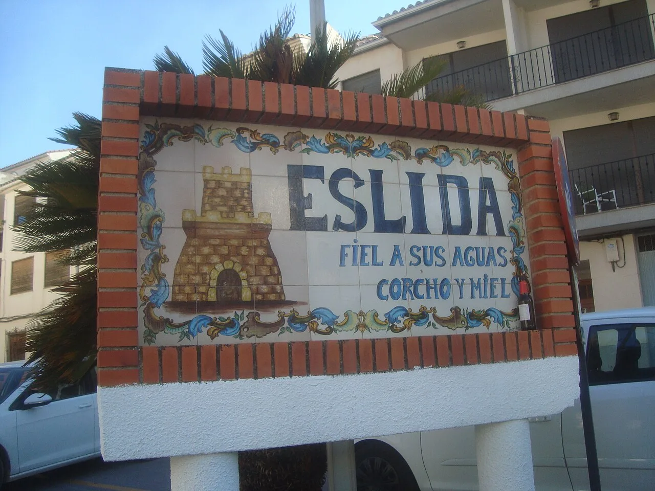 Cartel con el eslogan mural de Eslida, con torre y decoración colorida.