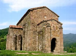 Kirche Santa Cristina de Lena in einer Landschaft mit Bergen und blauem Himmel.