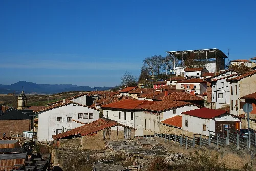 Weiße Häuser mit roten Dächern in Añana, mit einem großen Gebäude auf dem Hügel und Bergen im Hintergrund.