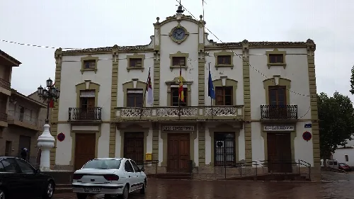 Edificio con fachada blanca y detalles en beige, con banderas en la entrada.