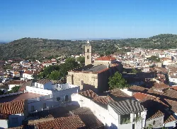 Church and houses in Montánchez, with hills and blue sky.