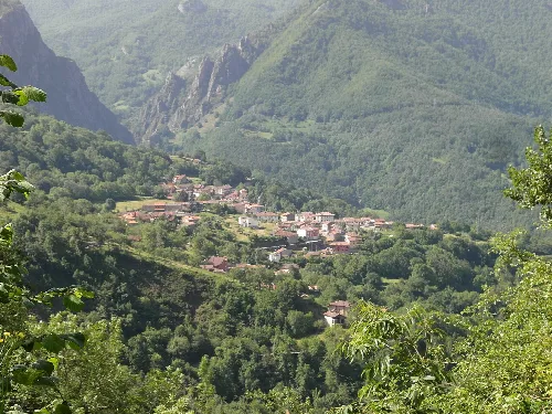 Landschaft mit Häusern in einem Tal, umgeben von grünen Bergen.