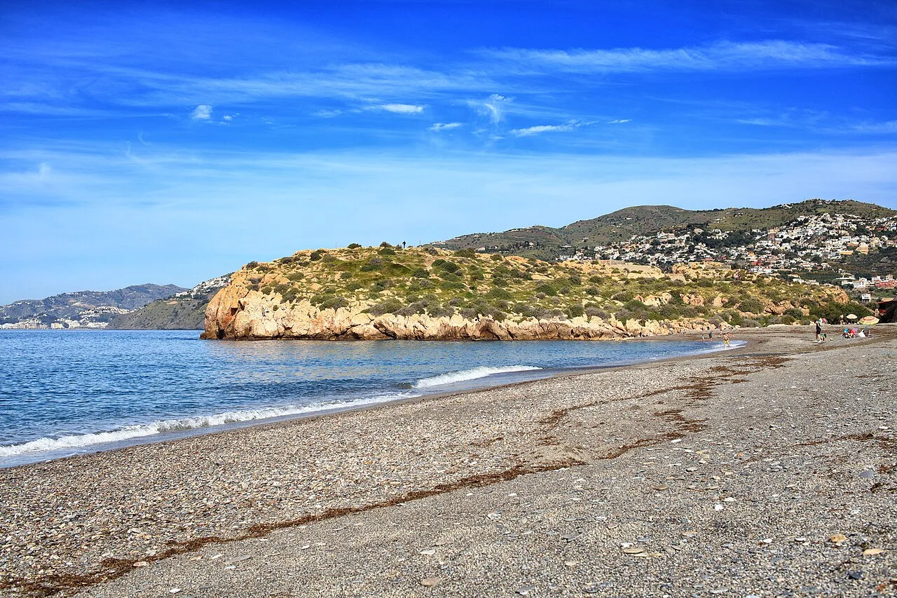 Beach with sand and blue water, rocky promontory and clear sky.