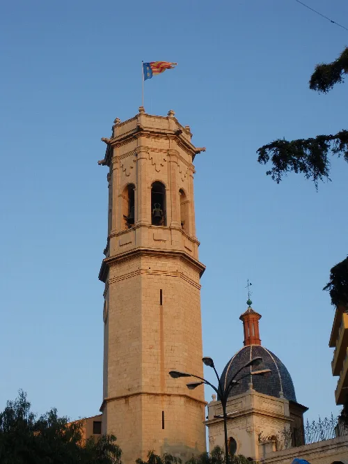 Stone bell tower with flag on top and blue sky.