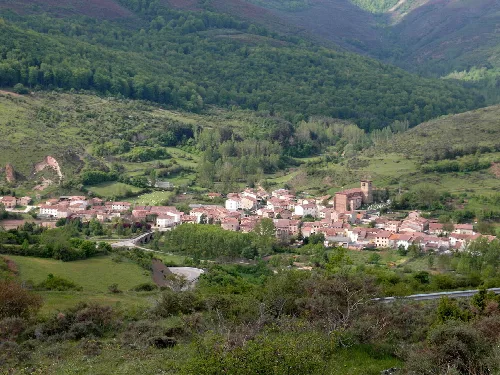 View of a village in a valley surrounded by mountains and greenery.