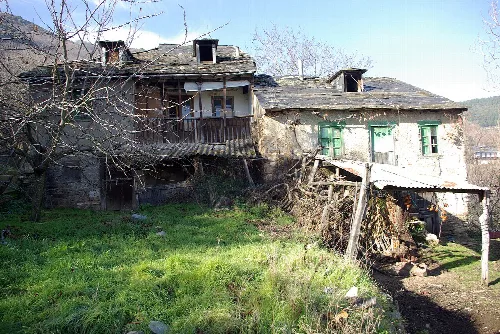 Altes Haus aus Stein und Holz in Corullón mit Grün und kahlen Bäumen.