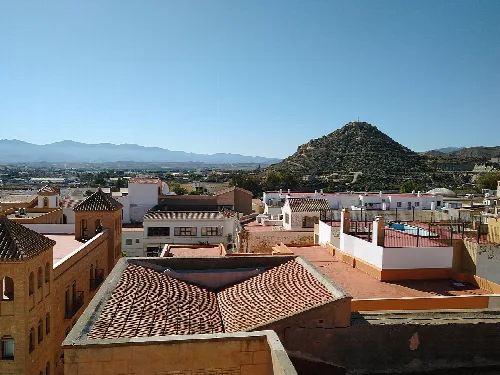 Tejados y casas en Vera con una colina en el fondo.