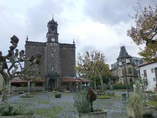 Iglesia de Ispáster con torre y reloj, en una plaza con árboles podados.