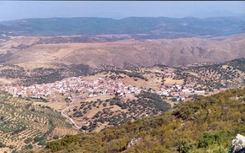 Blick auf ein Dorf in einem Tal, umgeben von Hügeln und Vegetation.
