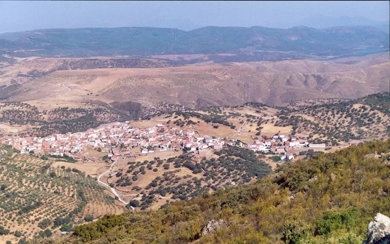 Blick auf ein Dorf in einem Tal, umgeben von Hügeln und Vegetation.