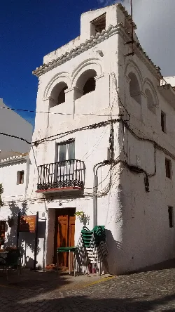 Edificio blanco con balcón y varias sillas apiladas en la calle.