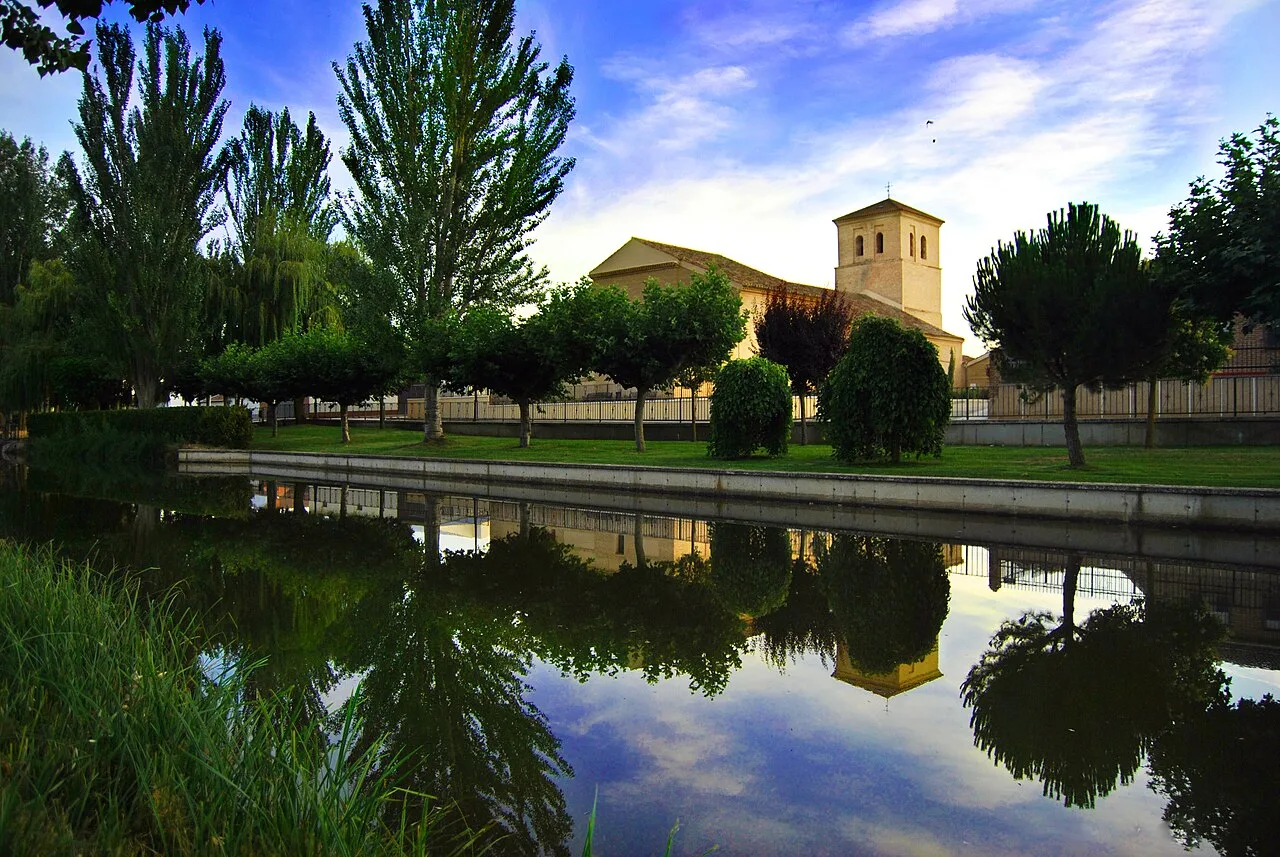 Iglesia de Santiago vista desde el cuérnago de La Perionda, con árboles y reflejo en el agua.