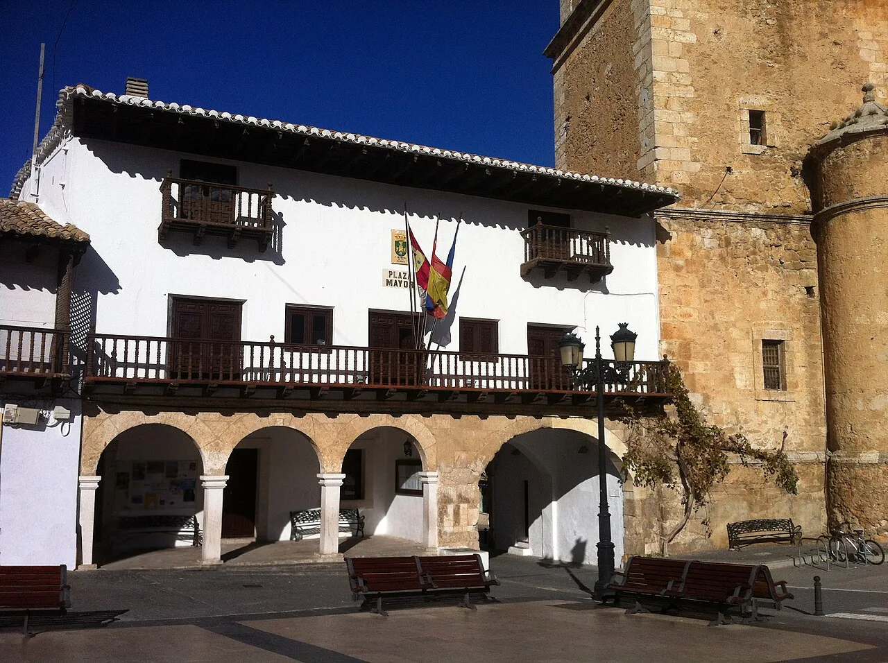Edificio blanco con arcos en la planta baja y balcones de madera en la fachada.