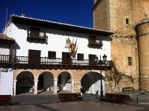 Edificio blanco con arcos en la planta baja y balcones de madera en la fachada.