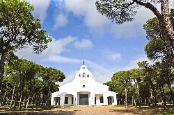 Weiße Kapelle, umgeben von Bäumen und Himmel mit Wolken.