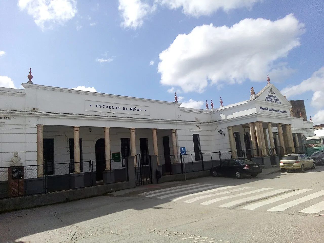Edificio blanco de escuela con columnas y cartel en la fachada.