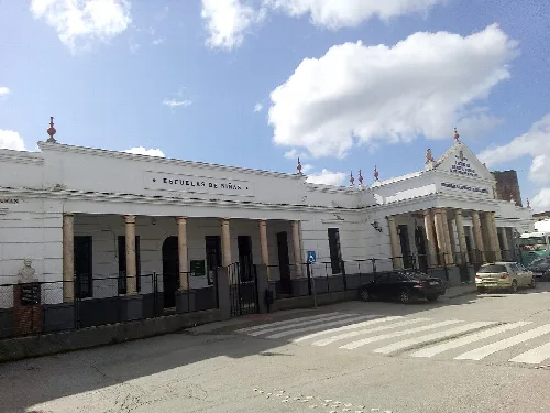 Weißes Schulgebäude mit Säulen und Schild an der Fassade.