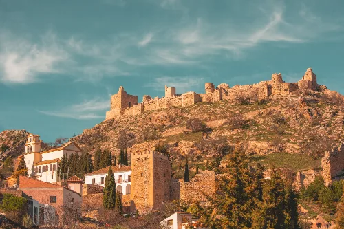Blick auf die Burg von Moclín in Granada auf einem Hügel mit Häusern und Bäumen drumherum.