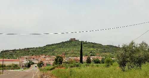 Landschaft mit Burg auf dem Hügel und Dorf im Tal.