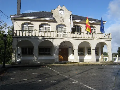 Weißes Gebäude mit Bögen im Erdgeschoss und einer Uhr oben.